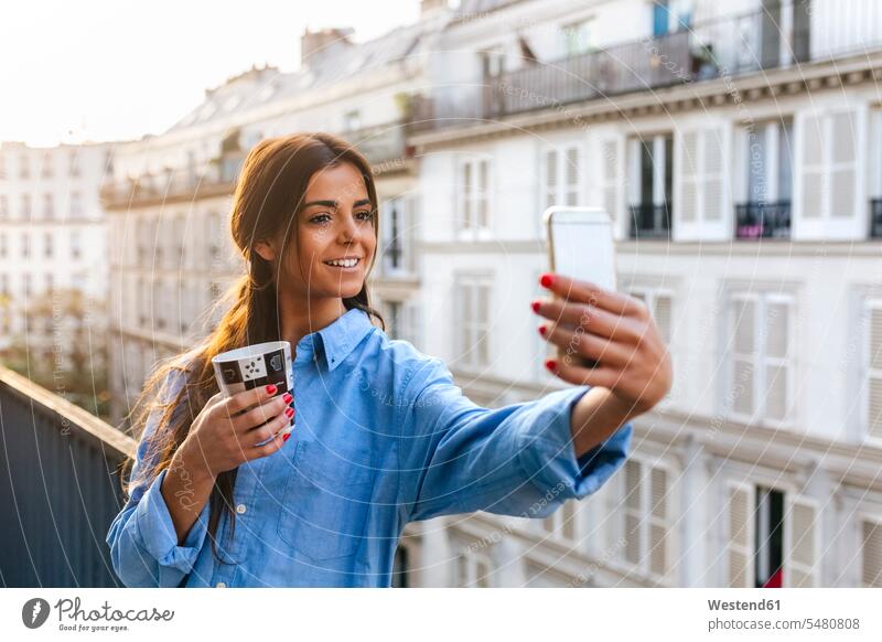 Junge Frau steht auf einem Balkon und macht ein Selfie mit ihrem Smartphone weiblich Frauen jung benutzen benützen Balkone Kaffee Kaffeetasse Kaffeetassen