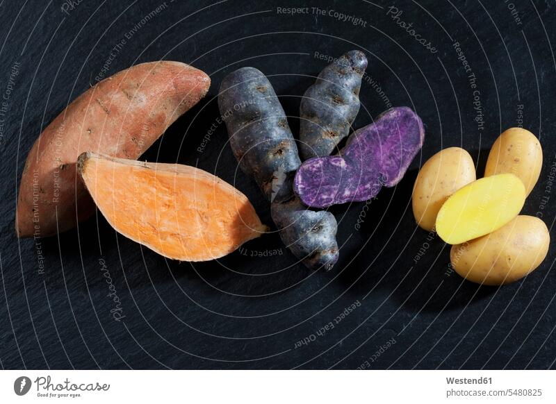 Ganze und in Scheiben geschnittene Süßkartoffel, Purpurkartoffel und Drillinge auf Schiefer lila lilafarben violett ungekocht roh aufgeschnitten angeschnitten