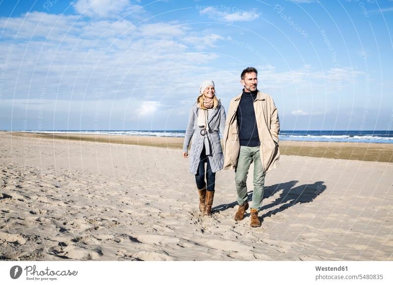 Paar in warmer Kleidung beim Spaziergang am Strand Beach Straende Strände Beaches lächeln Pärchen Paare Partnerschaft Mensch Menschen Leute People Personen