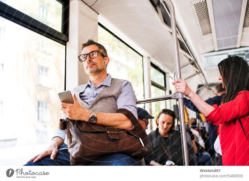 Geschäftsmann mit Smartphone und Kopfhörern in der Straßenbahn unterwegs Mann Männer männlich Trambahn S-Bahn S-Bahnen Strassenbahnen Straßenbahnen Handy