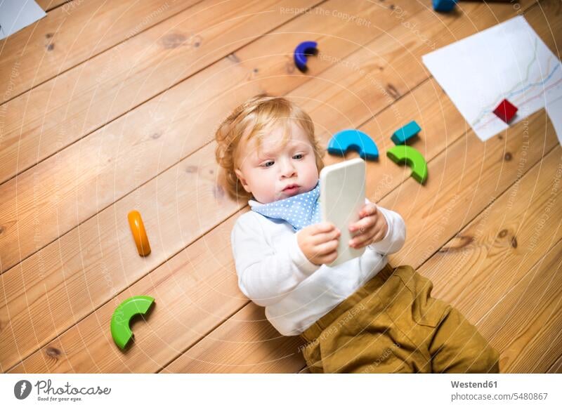 Kleiner Junge zu Hause spielt mit Smartphone spielen liegen liegend liegt Handy Mobiltelefon Handies Handys Mobiltelefone Telefon telefonieren Kommunikation