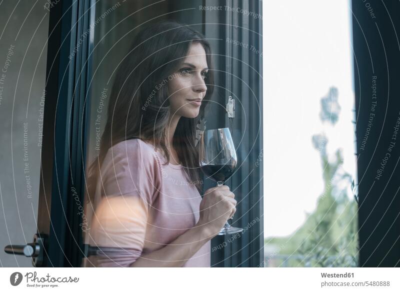 Lächelnde Frau hält ein Glas Rotwein und schaut aus dem Fenster Rotweine entspannt entspanntheit relaxt lächeln weiblich Frauen Wein Weine Alkohol