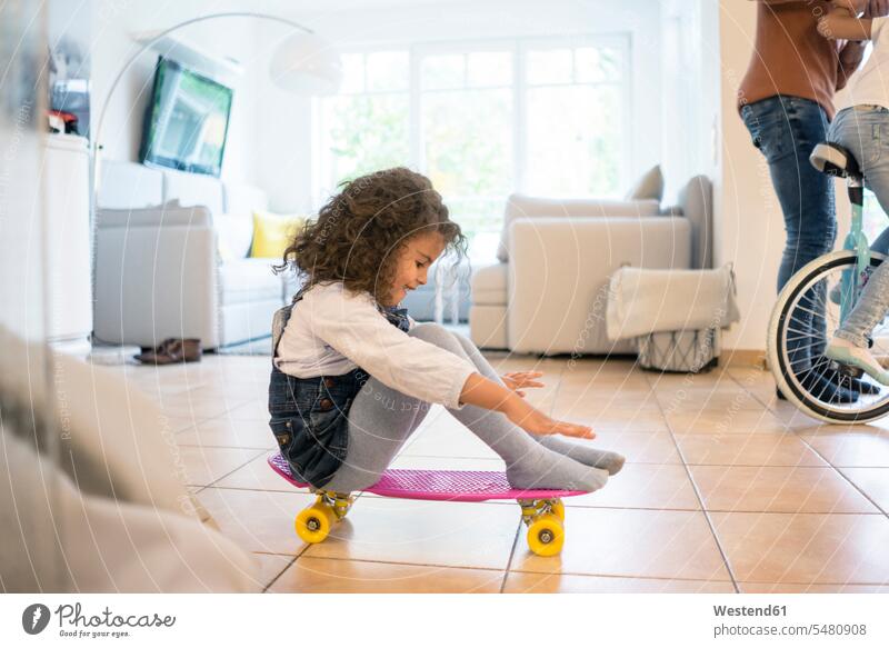 Kleines Mädchen sitzt auf einem Skateboard und hat Spaß Wohnzimmer Wohnraum Wohnung Wohnen Wohnräume Wohnungen sitzen sitzend spielen lernen balancieren Balance