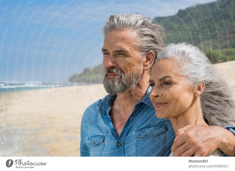 Porträt eines hübschen älteren Ehepaares am Meer umarmen Umarmung Umarmungen Arm umlegen Senioren alte Strand Beach Straende Strände Beaches Urlaub Ferien