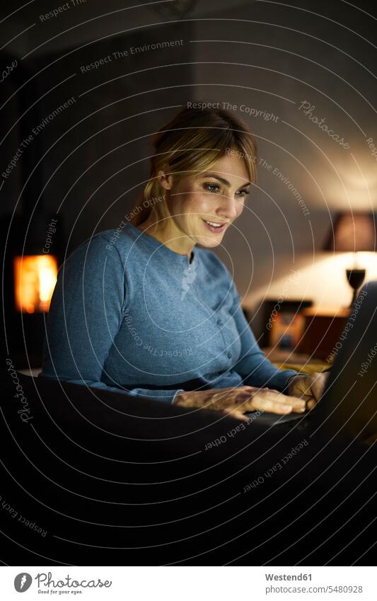 Porträt einer lächelnden Frau, die abends zu Hause einen Laptop benutzt Abend weiblich Frauen Zuhause daheim Portrait Porträts Portraits benutzen benützen