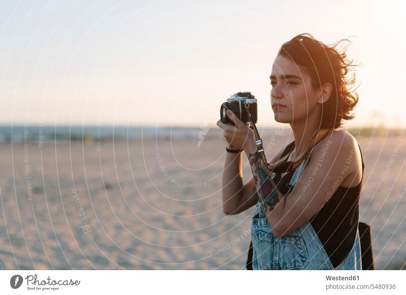 USA, New York, Coney Island, junge Frau beim Fotografieren am Strand bei Sonnenuntergang Kamera Kameras suchen Suche Oberkörper Oberkörperaufnahmen Halbfigur