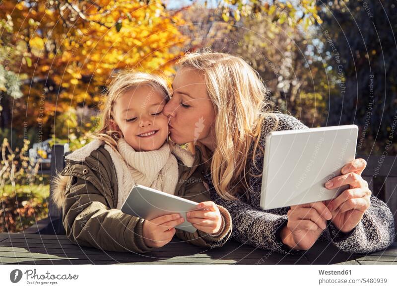 Mutter mit Tochter am Gartentisch mit Tablette und Handy Töchter Mami Mutti Mütter Mama glücklich Glück glücklich sein glücklichsein lächeln Mobiltelefon