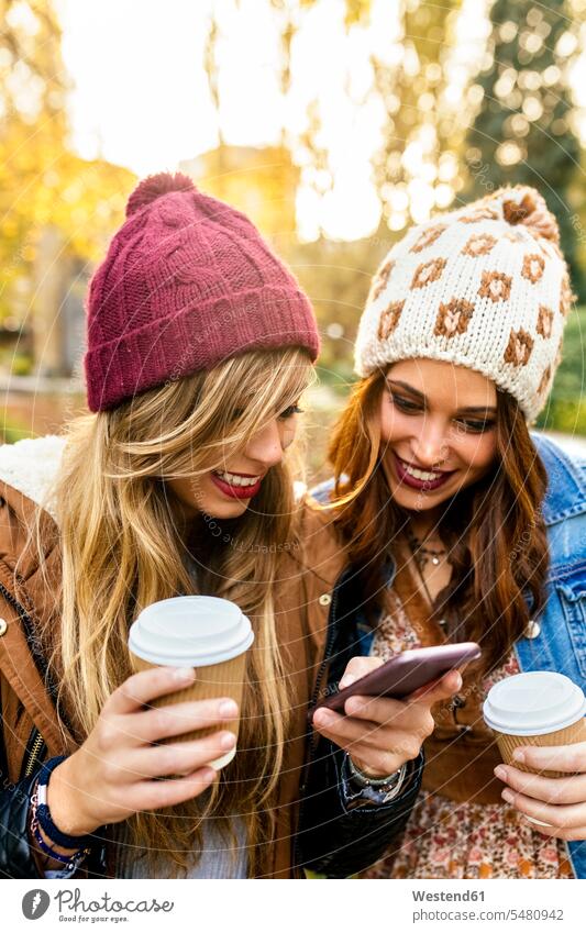 Zwei junge Frauen mit Smartphone in einem Park im Herbst Parkanlagen Parks Handy Mobiltelefon Handies Handys Mobiltelefone lächeln Freundinnen Telefon