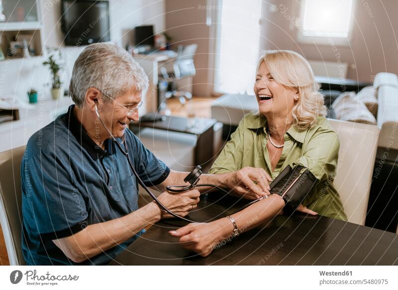 Glückliches älteres Ehepaar bei der Blutdruckmessung Paar Pärchen Paare Partnerschaft Senior ältere Männer älterer Mann Senioren lachen Mensch Menschen Leute