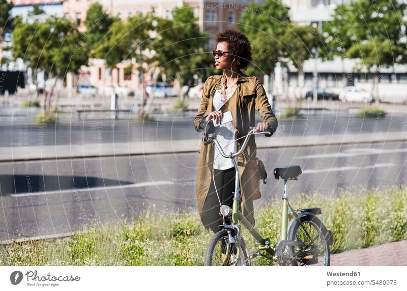 Junge Frau mit Smartphone und Kopfhörern schiebt Fahrrad weiblich Frauen Bikes Fahrräder Räder Rad Erwachsener erwachsen Mensch Menschen Leute People Personen
