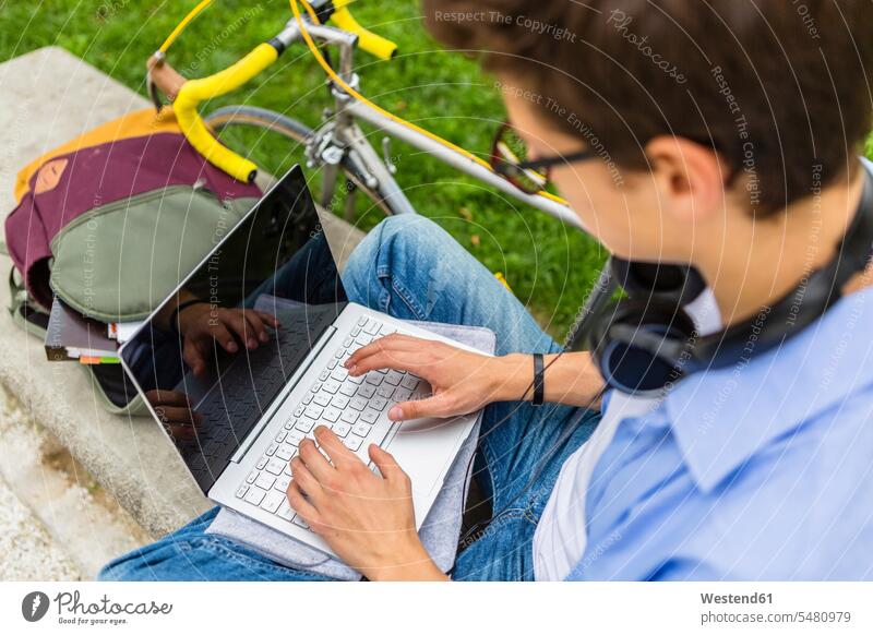 Junger Mann mit Rennrad, der auf einer Bank sitzt und einen Laptop benutzt, gelockerte Sicht Männer männlich Notebook Laptops Notebooks Erwachsener erwachsen