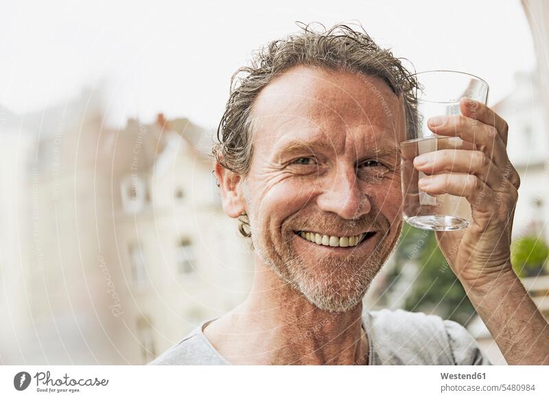 Porträt eines lächelnden Mannes, der mit einem Wasserglas anstößt zuprosten Glas Trinkgläser Gläser Trinkglas Portrait Porträts Portraits trinken Balkon Balkone