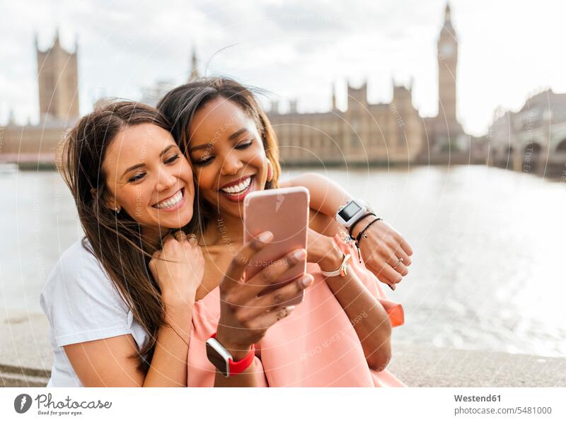 UK, London, zwei glückliche Frauen mit Smartphone in der Nähe der Westminster Bridge weiblich Selfie Selfies Freundinnen lächeln Handy Mobiltelefon Handies