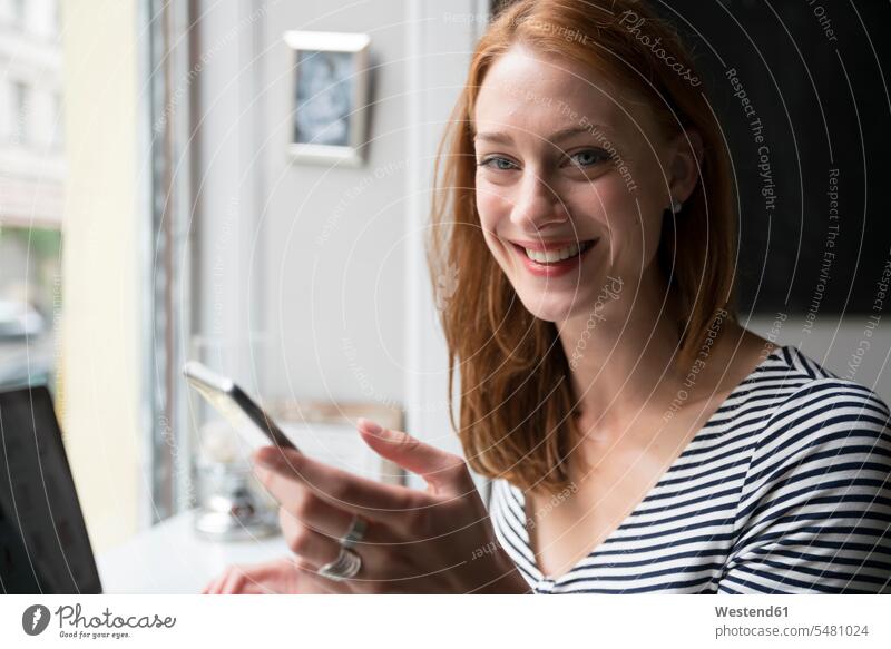 Porträt einer rothaarigen Frau mit Smartphone in einem Café Portrait Porträts Portraits lächeln iPhone Smartphones weiblich Frauen Handy Mobiltelefon Handies