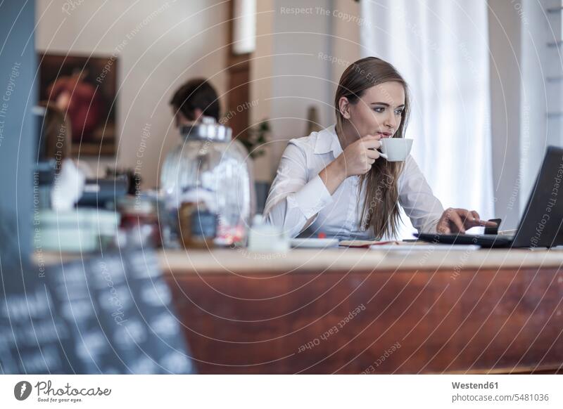 Junge Frau sitzt an der Kaffeebar, arbeitet und trinkt Kaffee Europäer Kaukasier Europäisch kaukasisch Verbindung verbunden verbinden Anschluss Kaffeetasse