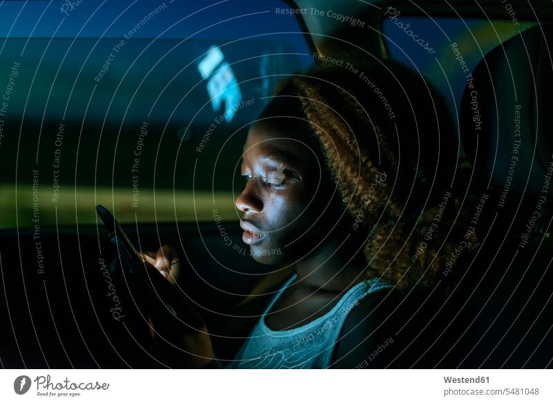 Junge Frau, die nachts im Auto ein Smartphone benutzt Wagen PKWs Automobil Autos Handy Mobiltelefon Handies Handys Mobiltelefone weiblich Frauen Kraftfahrzeug