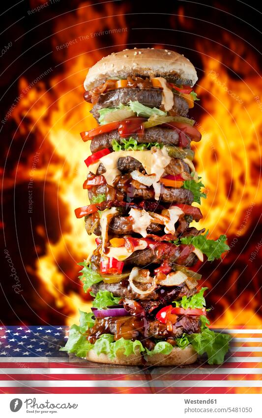 Extra großer Hamburger auf US-Flagge gegen brennende Flamen Rindfleisch Käse Kaese Saure Gurke Saure Gurken Salzgurken Essiggurken Gewürzgurke Gewürzgurken