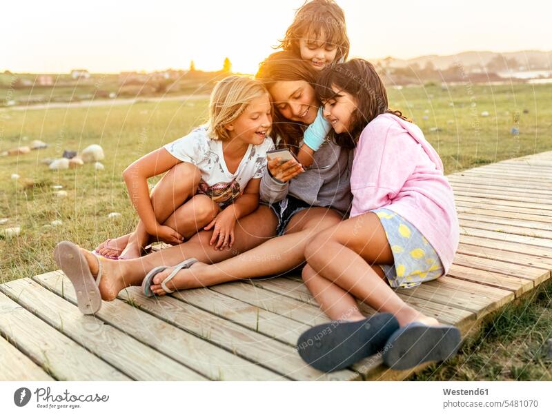 Vier Mädchen sitzen zusammen auf der Strandpromenade und schauen auf ihr Handy weiblich Freundinnen Smartphone iPhone Smartphones Kind Kinder Kids Mensch