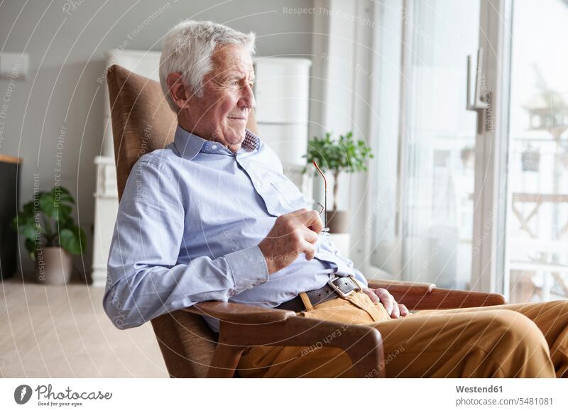 Porträt eines älteren Mannes, der zu Hause auf einem Sessel sitzt und durch ein Fenster schaut Europäer Kaukasier Europäisch kaukasisch Zuversicht