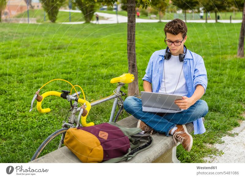 Junger Mann mit Rennrad, der mit einem Laptop auf einer Bank sitzt Notebook Laptops Notebooks Männer männlich Computer Rechner Erwachsener erwachsen Mensch