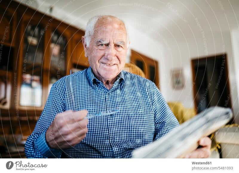 Porträt eines lächelnden älteren Mannes mit Zeitung zu Hause Europäer Kaukasier Europäisch kaukasisch Zuversicht Zuversichtlich Selbstvertrauen selbstbewusst