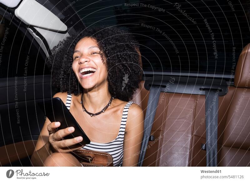 Porträt einer lachenden Frau mit Smartphone, die auf den Rücksitzen eines Autos sitzt iPhone Smartphones Wagen PKWs Automobil weiblich Frauen Handy Mobiltelefon