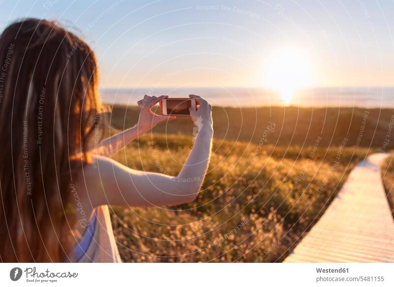 Junge Frau fotografiert Strand bei Sonnenuntergang mit Smartphone fotografieren Handy Mobiltelefon Handies Handys Mobiltelefone iPhone Smartphones jung Beach