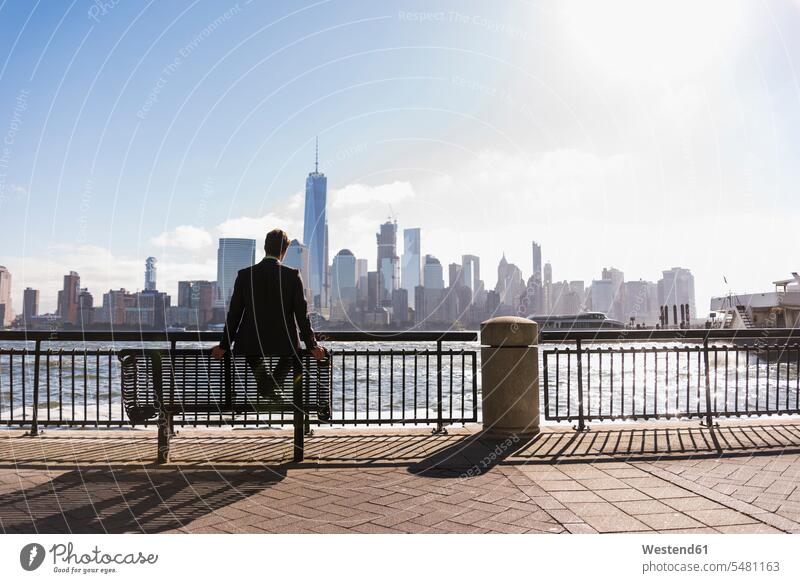 USA, Mann sitzt auf einer Bank am Hafen von New Jersey mit Blick auf Manhattan lächeln sitzen sitzend Männer männlich New York New York State Sitzbänke Bänke