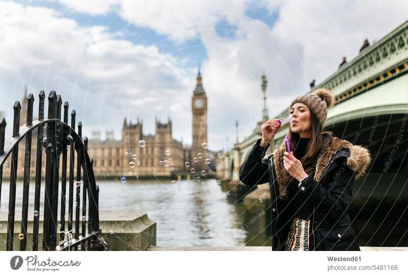 UK, London, junge Frau, die Seifenblasen pustet Seifenblasenring Seifenblasenringe Städtereise City Trip Kurztripp City Break Wollmütze Wollmützen Strickmütze