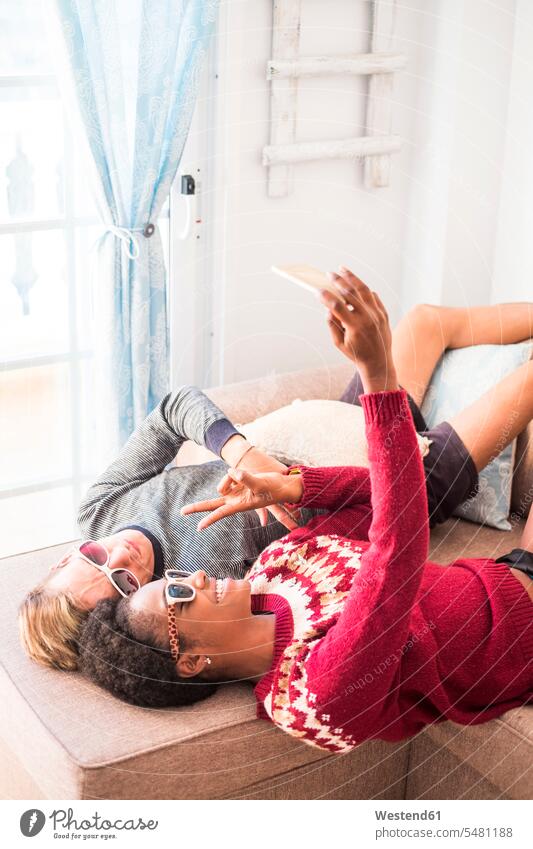 Junges Paar mit Sonnenbrille macht Selfie auf der Couch Selfies Pärchen Paare Partnerschaft liegen liegend liegt Mensch Menschen Leute People Personen