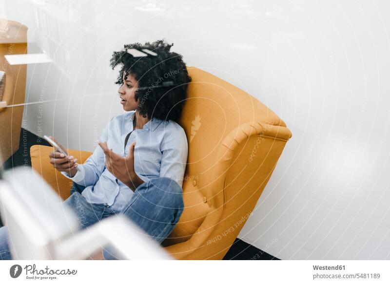 Junge Frau mit Handy im Sessel sitzend weiblich Frauen sitzt Mobiltelefon Handies Handys Mobiltelefone Stuhl Stuehle Stühle Erwachsener erwachsen Mensch