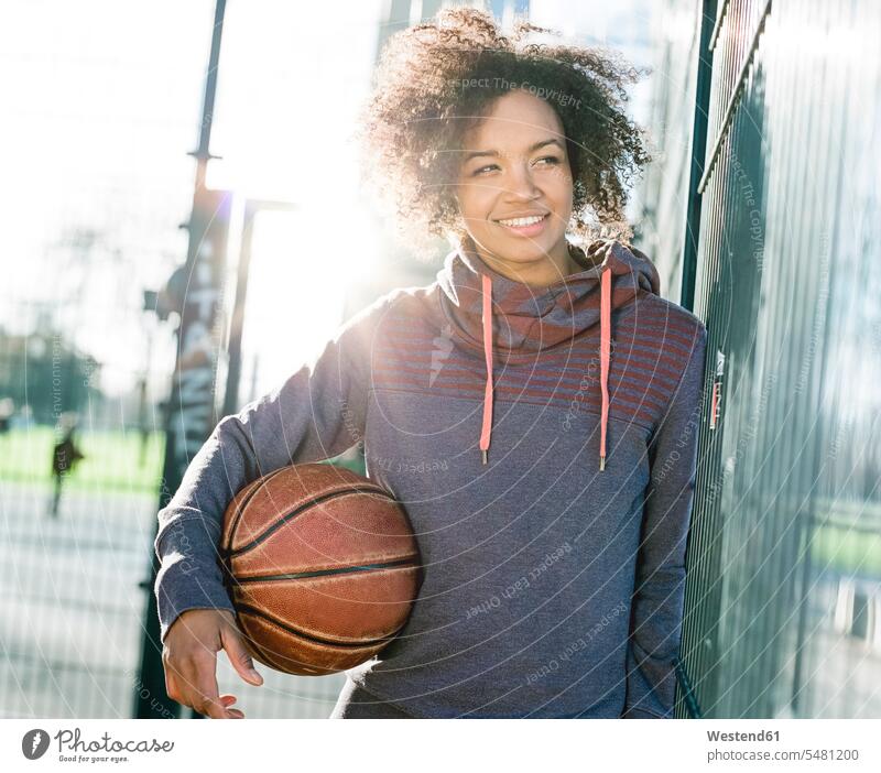 Porträt einer lächelnden jungen Frau mit Basketball im Gegenlicht gemischtrassige Person sportlich Linsenreflexion Blendenflecken Reflexlicht Lens Flare Himmel