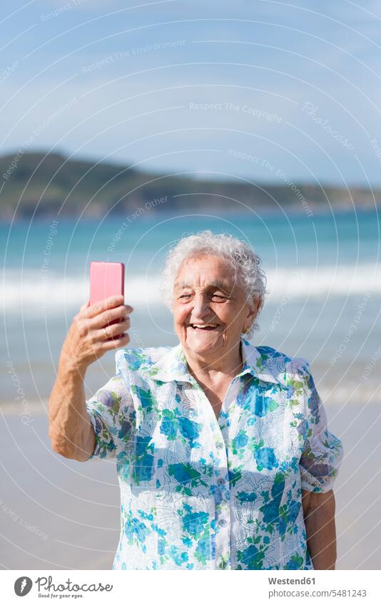Glückliche ältere Frau nimmt Selfie am Strand Selfies Seniorin Seniorinnen alt fotografieren Senioren weiblich Frauen Erwachsener erwachsen Mensch Menschen