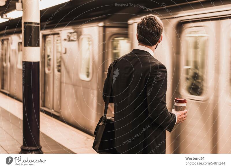 Junger Geschäftsmann wartet am Bahnsteig der U-Bahn-Station und hält Einwegbecher Businessmann Businessmänner Geschäftsmänner Zugbahnsteig Zugbahnsteige