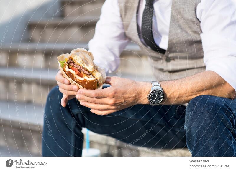 Geschäftsmann in der Stadt sitzt auf einer Treppe und isst einen Hamburger Businessmann Businessmänner Geschäftsmänner Pause Treppenaufgang Burger