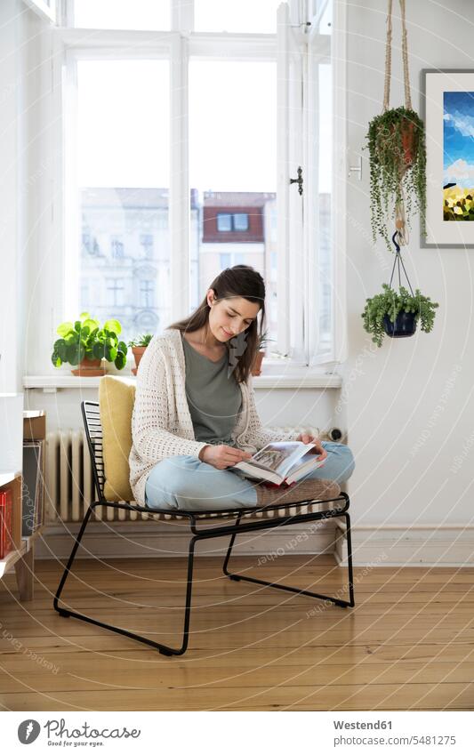 Frau zu Hause sitzt auf Stuhl und liest Buch sitzen lesen Erwachsener Mensch Zuhause Wohnzimmer Studentin lächeln Tag Innenaufnahme Deutschland Vorderansicht