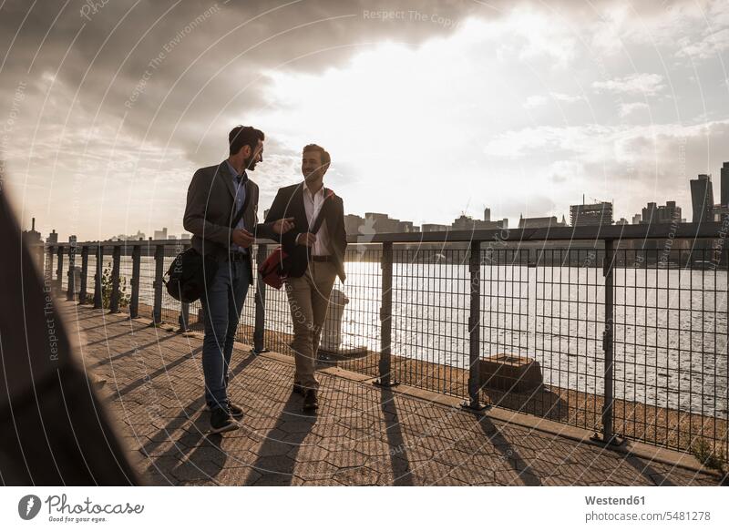 USA, New York City, zwei Geschäftsleute gehen am East River entlang Mann Männer männlich lächeln gehend geht Geschäftsmann Businessmann Businessmänner