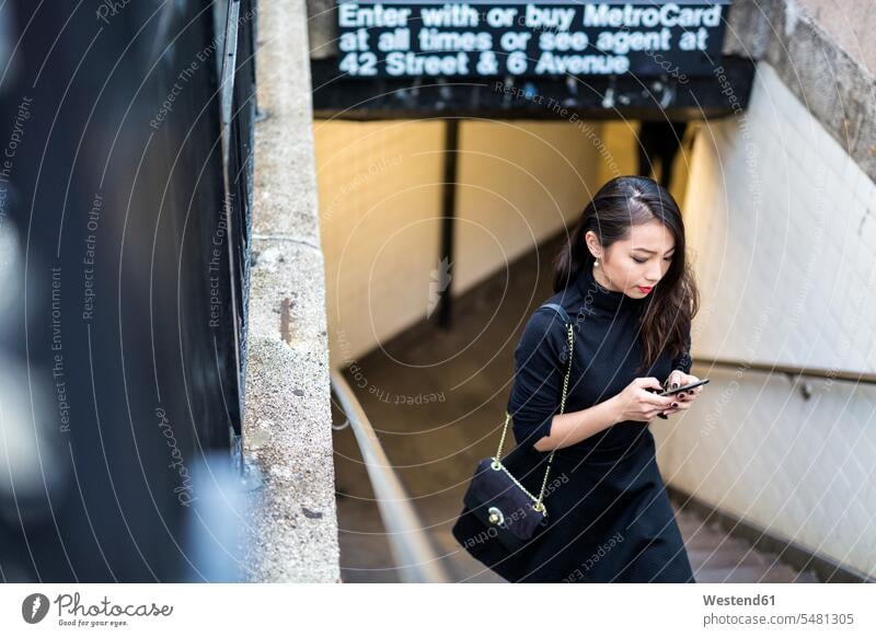USA, New York City, Manhattan, junge Frau in Schwarz gekleidet, die eine Treppe hinaufgeht weiblich Frauen Smartphone iPhone Smartphones Erwachsener erwachsen