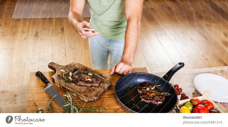 Mann mit zubereiteten Steaks in der Küche mit Mobiltelefon Europäer Kaukasier Europäisch kaukasisch Deutschland Innenaufnahme drinnen Innenaufnahmen