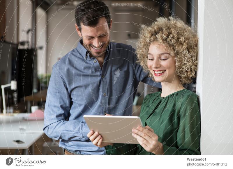 Lächelnder Mann und Frau betrachten Tablette im Büro Kollegen Arbeitskollegen Office Büros Tablet Computer Tablet-PC Tablet PC iPad Tablet-Computer lächeln
