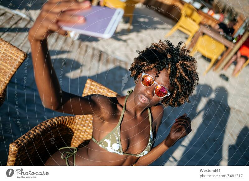 Junge Frau macht ein Selfie mit einem Smartphone in einer Strandbar Selfies Beach Straende Strände Beaches weiblich Frauen Erwachsener erwachsen Mensch Menschen