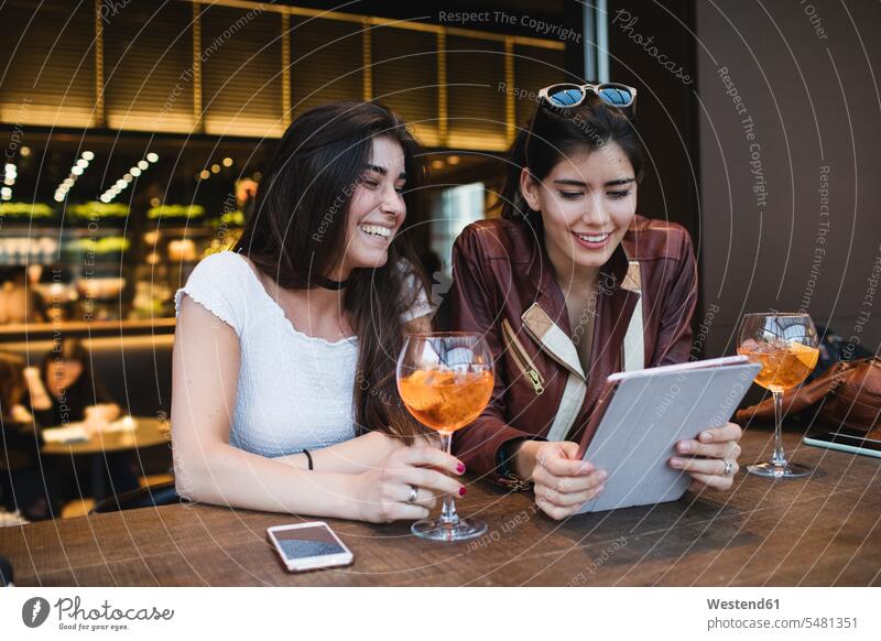 Zwei glückliche junge Frauen betrachten Tablette in einer Bar Tablet Computer Tablet-PC Tablet PC iPad Tablet-Computer Freundinnen lächeln Rechner Freunde