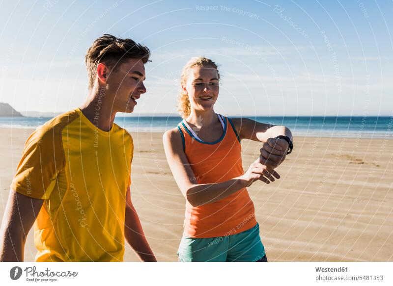 Frankreich, Halbinsel Crozon, sportliches junges Paar am Strand, das auf die Uhr schaut Armbanduhr Armbanduhren Beach Straende Strände Beaches Pärchen Paare