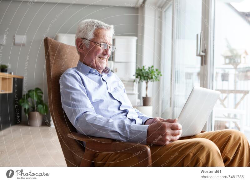 Porträt eines älteren Mannes, der zu Hause auf einem Sessel sitzt und einen Laptop benutzt Europäer Kaukasier Europäisch kaukasisch Zuversicht Zuversichtlich