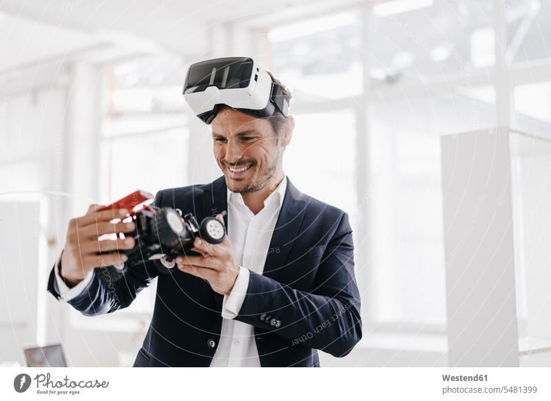 Lächelnder Geschäftsmann mit VR-Brille schaut Spielzeug-Rennwagen an 3D Brille 3D-Brille Mann Männer männlich Businessmann Businessmänner Geschäftsmänner