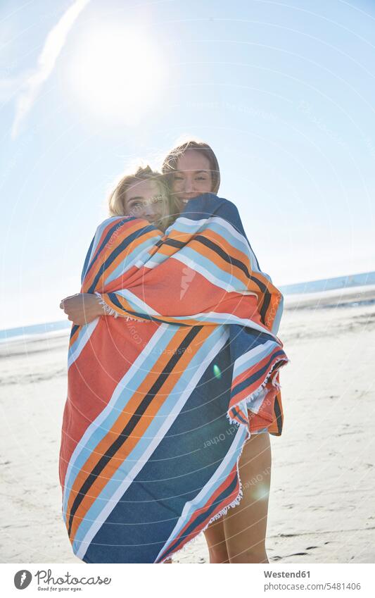 Zwei junge Frauen in eine Decke gehüllt am Strand weiblich Freundinnen Decken lächeln Urlaub Ferien Beach Straende Strände Beaches Erwachsener erwachsen Mensch