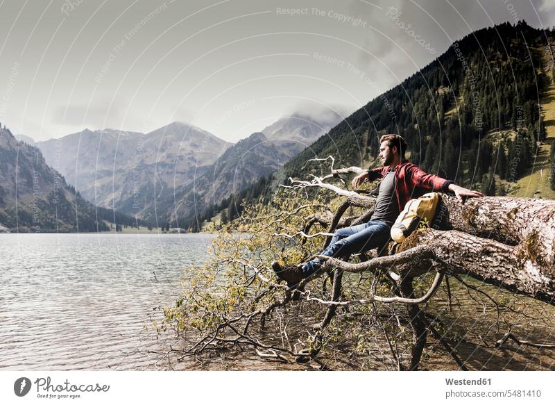 Österreich, Tirol, Alpen, Wanderer auf Baumstamm am Bergsee entspannen Stamm Stämme Baumstämme See Seen Mann Männer männlich sitzen sitzend sitzt Bäume Baeume