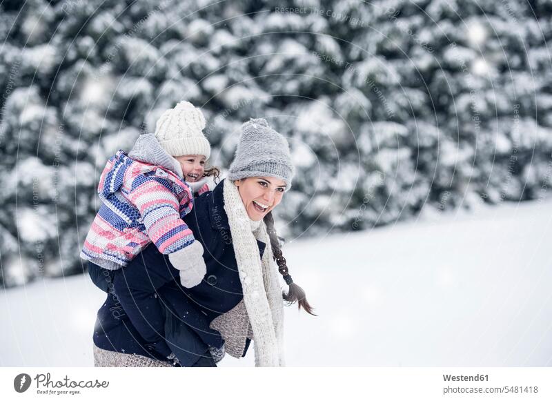 Glückliche Mutter trägt Tochter huckepack in Winterlandschaft Töchter tragen transportieren winterlich Winterzeit lachen Mami Mutti Mütter Mama Kind Kinder