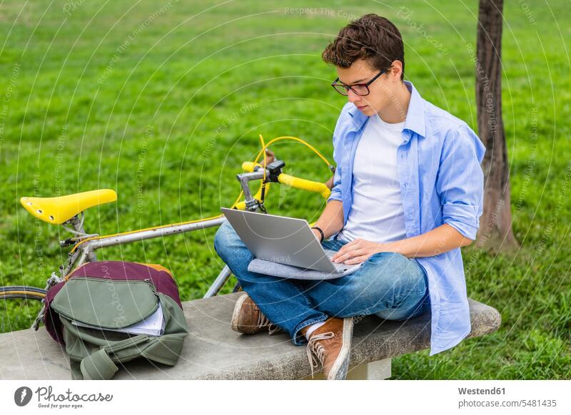 Junger Mann mit Rennrad, der mit einem Laptop auf einer Bank sitzt Notebook Laptops Notebooks Männer männlich Computer Rechner Erwachsener erwachsen Mensch