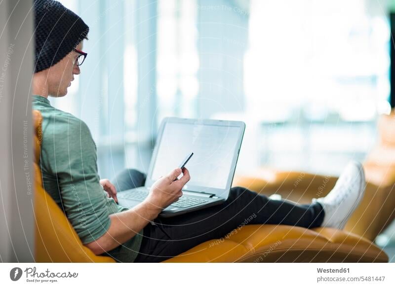 Junger Mann arbeitet im Sessel, benutzt Laptop Notebook Laptops Notebooks arbeiten Arbeit sitzen sitzend sitzt Konzentration konzentriert konzentrieren Männer